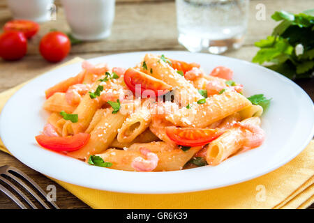 Pâtes penne aux crevettes, sauce tomate, le persil et le parmesan râpé sur fond de bois rustique Banque D'Images