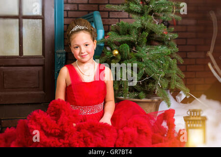 Cute little girl in red dress accueille la nouvelle année et de Noël Noël enchanteur pin décoré avec de l'intérieur Banque D'Images