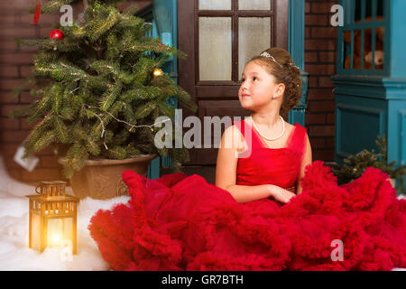 Cute little girl in red dress se félicite de nouvel an et de Noël en vacances enchanteresses avec arbre de Noël la décoration d'intérieur Banque D'Images