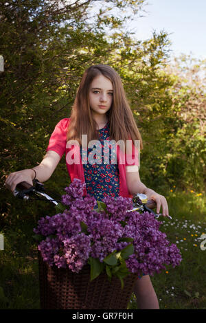 Teenage girl sitting on un vélo avec un panier de fleurs à tout droit à l'appareil photo Banque D'Images