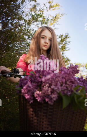 Teenage girl sitting on un vélo avec un panier de fleurs à tout droit à l'appareil photo Banque D'Images