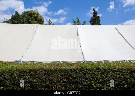 Une grande tente blanche ou chapiteau, caché derrière une haie de jardin. Banque D'Images