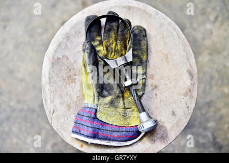 Le gant du travailleur sale tenant une clé de filtre à huile sur une planche en bois dans un atelier Banque D'Images