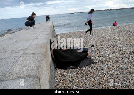 Couple sur la plage assis par mur de béton à la recherche au niveau d'une caméra sur la plage à Lyme Regis, dans le Dorset, Angleterre Royaume-uni KATHY DEWITT Banque D'Images