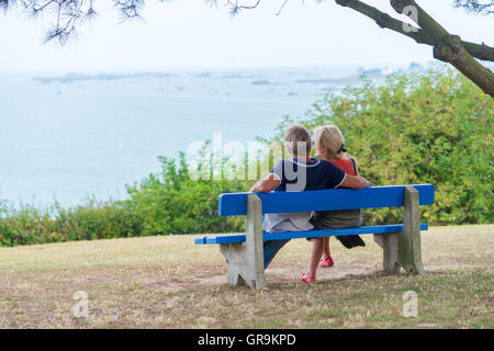 Couple assis sur un banc bleu et regarde la mer Banque D'Images