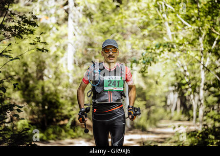 L'âge de l'athlète masculin midlife fonctionne en bois avec poteaux nordique dans la main pendant le marathon de montagne Banque D'Images