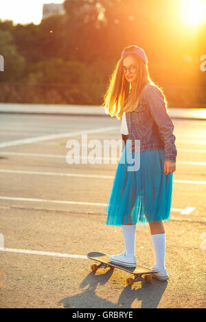 La mode de vie, très belle jeune femme avec skateboard, rétroéclairé au coucher du soleil Banque D'Images