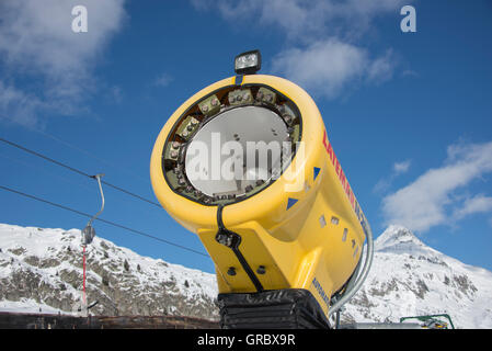 Canon à neige jaune inactifs contre le ciel bleu, dans l'arrière-plan de montagnes couvertes de neige Banque D'Images