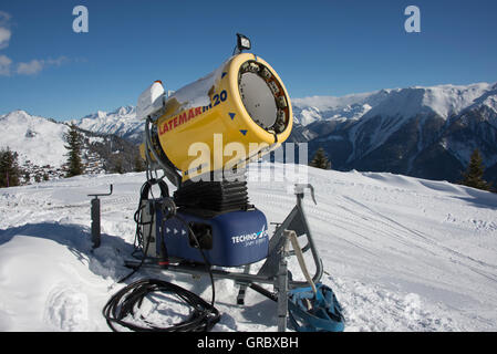 Canon à neige jaune inactifs contre le ciel bleu, dans l'arrière-plan de montagnes couvertes de neige Banque D'Images