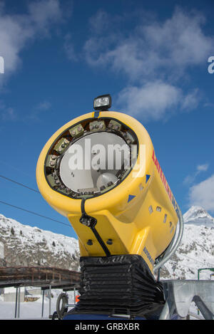 Canon à neige jaune inactifs contre le ciel bleu, dans l'arrière-plan de montagnes couvertes de neige Banque D'Images