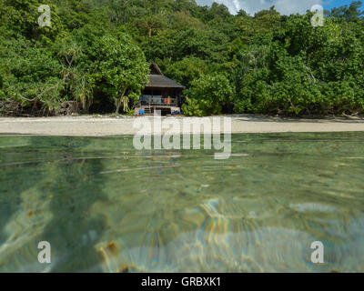 Plage de sable blanc, Bungalow de style traditionnel entouré de végétation tropicale, dans l'avant-plan d'eau de surface. Selayar, Sud de Sulawesi, Indonésie Banque D'Images