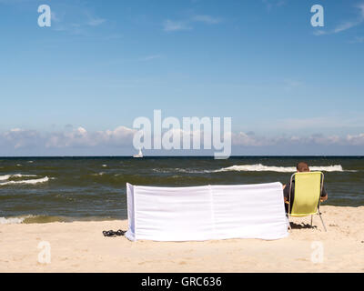 Sunbather détendue assis sur sunlonger jaune à côté du blanc coupe-vent à la plage Banque D'Images