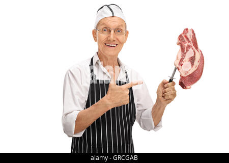 Personnes âgées butcher tenant une fourche à l'aide d'un morceau de viande crue sur elle et en montrant qu'il isolé sur fond blanc Banque D'Images