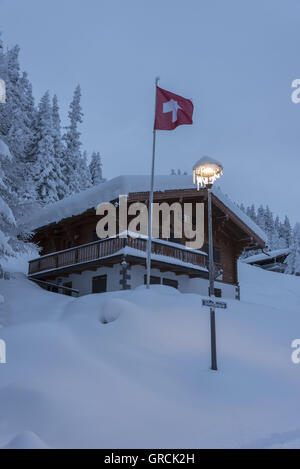 L'aube, Wintry Landscape avec forêt neige, Chalet, Icecled réverbère et agitant drapeau suisse. Banque D'Images