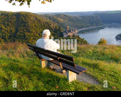 Homme assis sur un banc et regarde Burg Katz et la Loreley en arrière-plan, Rhin moyen Banque D'Images