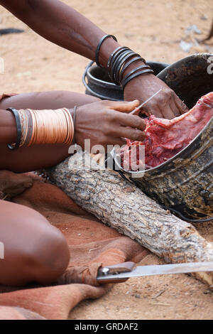 Femme Himba coupe la viande, prépare la nourriture, la Namibie, l'Afrique Banque D'Images