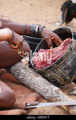Femme Himba coupe la viande, prépare la nourriture, la Namibie, l'Afrique Banque D'Images
