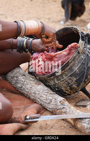 Femme Himba coupe la viande, prépare la nourriture, la Namibie, l'Afrique Banque D'Images