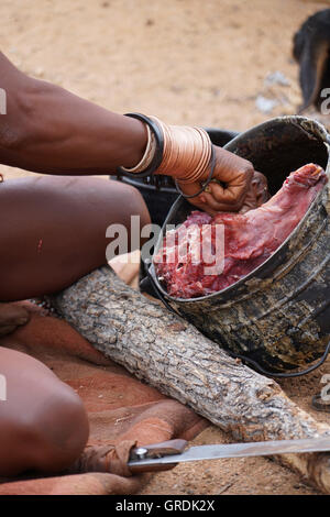 Femme Himba coupe la viande, prépare la nourriture, la Namibie, l'Afrique Banque D'Images