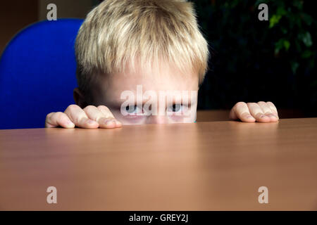 Triste garçon malheureux mécontents de se cacher sous la table pour enfants Banque D'Images