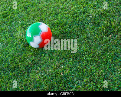 Ballon de soccer avec les couleurs du drapeau italien (vert, rouge, blanc) sur l'herbe d'un champ Banque D'Images