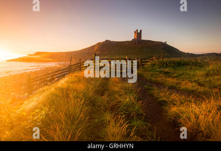 Lumière d'Aube dorée dans les ruines du château de Dunstanburgh, sur la côte de Northumberland, England UK Banque D'Images