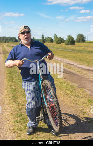 Funny senior montre qu'il était prêt à monter sur un vélo à country road Banque D'Images