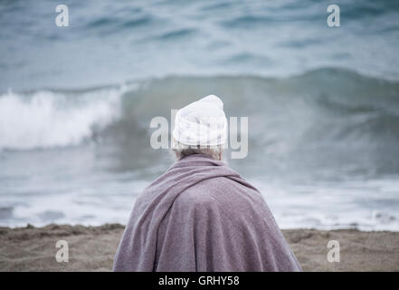 Un homme âgé portant turban assis sur la plage face à l'océan. Banque D'Images