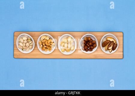 Les plats de dégustation contenant un assortiment de noix de cajou, pistaches, noix de macadamia et de noisette, noix du Brésil disposés en une rangée sur un boa en bois Banque D'Images