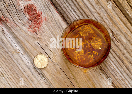 Verre de whisky et une pièce pour une gratification ou astuce debout sur un vieux comptoir de bar en bois texturé, vue du dessus avec copyspace Banque D'Images