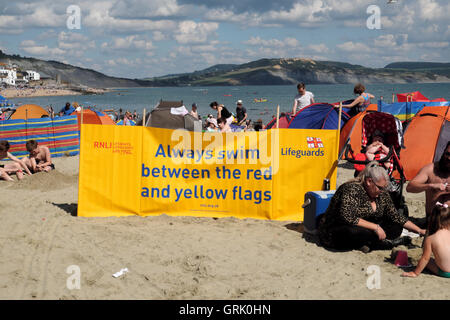 Les sauveteurs RNLI jaune bannière d'avertissement de sécurité de nager entre les drapeaux rouge et jaune sur la plage de Lyme Regis Dorset UK Banque D'Images