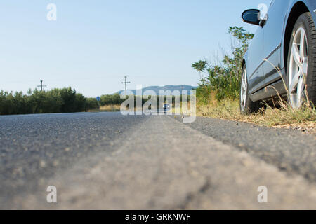 Voiture garée à côté d'une route dans les régions rurales du pays. Embuscade par voiture noire sur une route asphaltée. Vue d'un véhicule arrivant en sens inverse. Banque D'Images