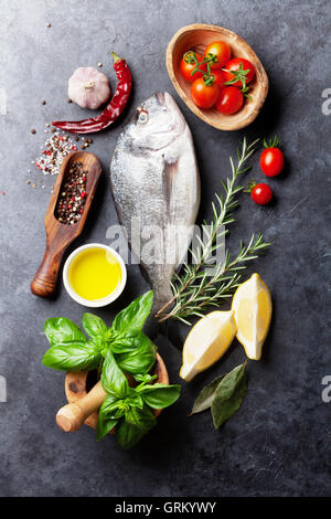 La cuisson du poisson cru et des ingrédients. Dorado, citron, herbes et épices. Vue de dessus sur table en pierre Banque D'Images