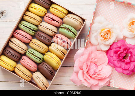 Macarons colorés et rose fleurs sur table en bois. Macarons sucrés en boîte cadeau. Vue d'en haut Banque D'Images