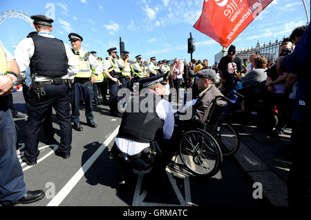 Un agent de police parle d'un protestataire sur le pont de Westminster au centre de Londres comme une démonstration a lieu contre les réductions des prestations d'invalidité. Banque D'Images