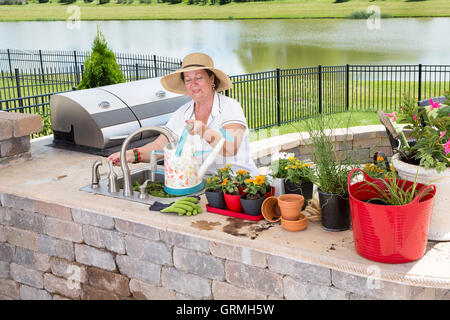 Dame âgée qui tend à ses plantes en pot du remplissage d'un arrosoir à l'évier dans son patio extérieur cuisine comme elle se prépare à Banque D'Images