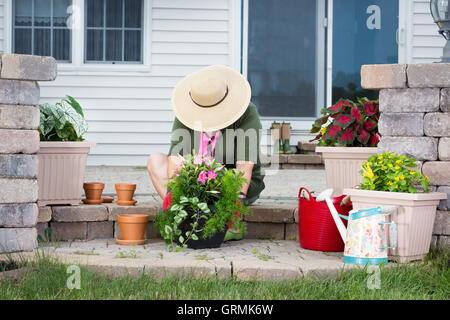 Dame âgée rempotage Des plantes d'une nouvelle assise sur les marches de son patio dans un chapeau à large chapeau en transplantant les plants Banque D'Images