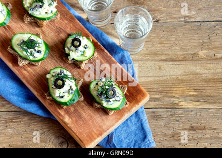 Mini-sandwiches (collations) avec le concombre, les olives et salade de poisson sur fond de bois rustique Banque D'Images