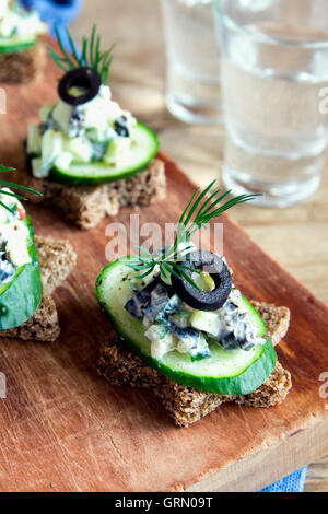 Mini-sandwiches (collations) avec le concombre, les olives et salade de poisson sur fond de bois rustique Banque D'Images