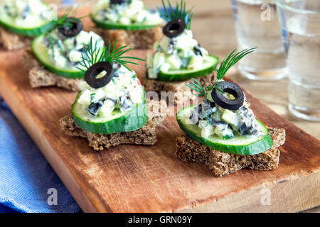 Mini-sandwiches (collations) avec le concombre, les olives et salade de poisson sur fond de bois rustique Banque D'Images