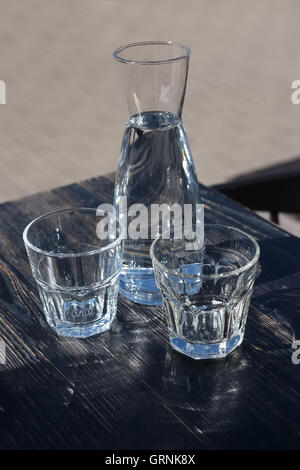 Deux verres et une bouteille d'eau sur une table en bois noir d'une terrasse de café Banque D'Images