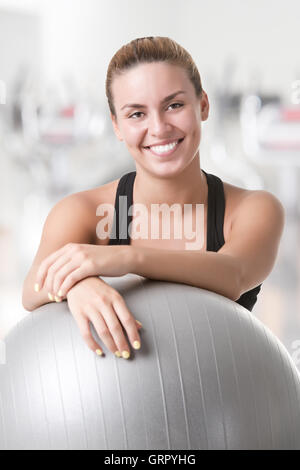 Fit woman sitting et tenant une balle Pilates au sol, dans une salle de sport Banque D'Images