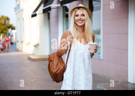 Smiling cheerful blonde girl in white dress holding à emporter à l'extérieur de la coupe Banque D'Images