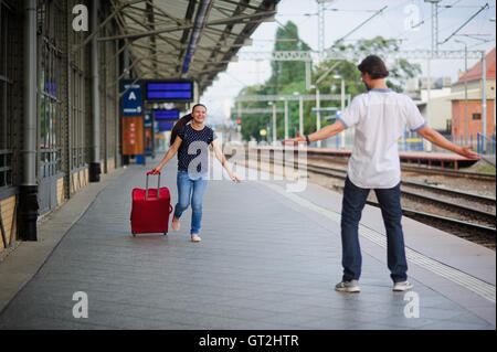 Lors d'une plate-forme vide fuir une jeune femme avec une valise rouge. Sourire joyeux sur son visage. Le jeune homme rencontre son. Il est prêt à hu Banque D'Images