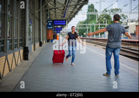 Lors d'une plate-forme vide fuir une jeune femme avec une valise rouge. Sourire joyeux sur son visage. Le jeune homme rencontre son. Il est prêt à hu Banque D'Images