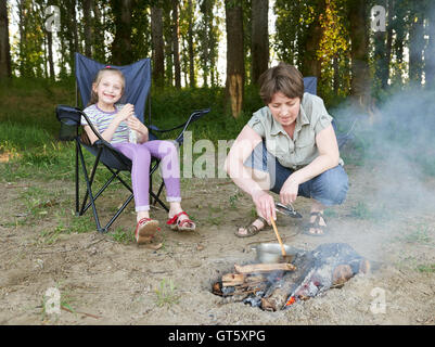 Femme à la cuisson des aliments, les gens du camping en forêt, dans la nature active de la famille, la jeune fille s'asseoir dans le siège de voyage, saison d'été Banque D'Images