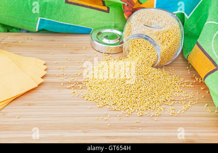 Grains de mil dans un bocal en verre avec des serviettes sur une planche en bois Banque D'Images