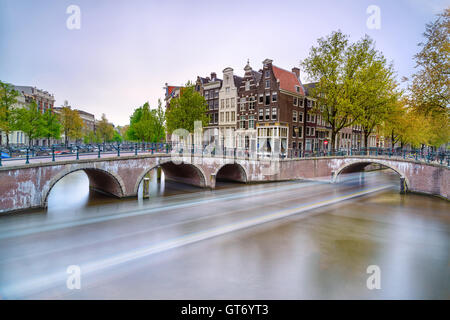 Amsterdam. L'eau et pont canal. Sentier lumineux bateau des temps d'exposition sur le coucher du soleil. La Hollande ou aux Pays-Bas. L'Europe. Banque D'Images