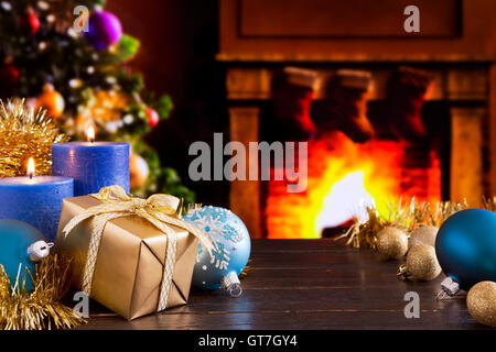 Décorations de Noël, un cadeau et des bougies devant une cheminée. Un feu brûle dans la cheminée et des bas de Noël ar Banque D'Images