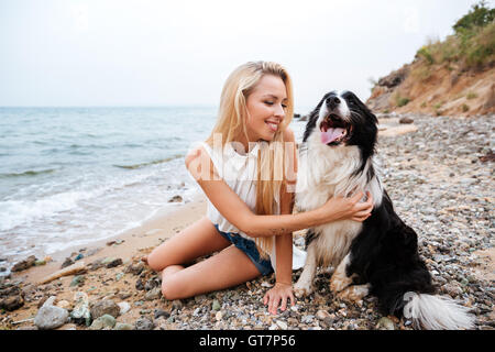 Cheerful charmante jeune femme assise avec son chien sur la plage Banque D'Images